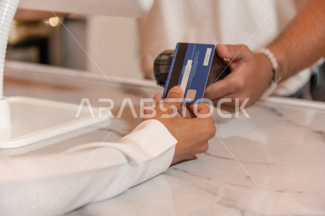 منظر من الخلف لرجل عربي سعودي خليجي يرتدي الثوب والشماغ السعودي, طلب القهوه من المقهى, الدفع عند الكاشير, الدفع الإلكتروني ببطاقة الصراف, مقاهي في المملكه العربيه السعوديه