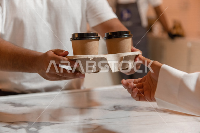 رجل عربي سعودي خليجي يستلم الطلب من المقهى, الطلب من متجر القهوه, تسليم القهوه للزبائن, الإستمتاع بشرب القهوه في المقهى, الدفع عند الكاشير, مقاهي في المملكه العربيه السعوديه