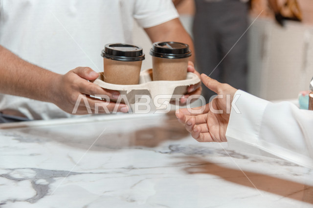 رجل عربي سعودي خليجي يستلم الطلب من المقهى, الطلب من متجر القهوه, تسليم القهوه للزبائن, الإستمتاع بشرب القهوه في المقهى, الدفع عند الكاشير, مقاهي في المملكه العربيه السعوديه