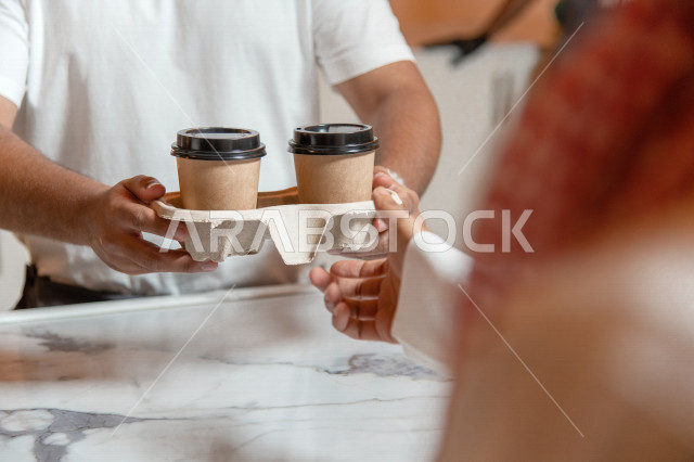 منظر من الخلف لرجل عربي سعودي خليجي يرتدي الثوب والشماغ السعودي, طلب القهوه من المقهى, إستلام القهوه, الإستمتاع بشرب القهوه في المقهى, الدفع عند الكاشير, مقاهي في المملكه العربيه السعوديه