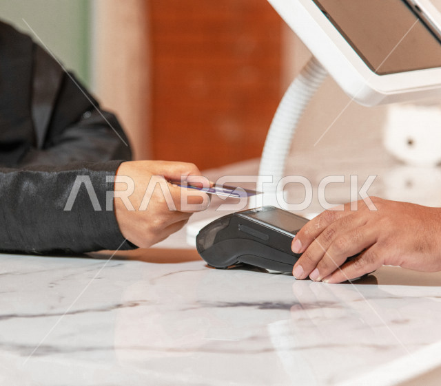 Saudi Arabian Gulf woman wearing hijab and abaya in the coffee shop, ordering coffee from the cafe, paying at the cashier, electronic payment with a teller card, cafes in the Kingdom of Saudi Arabia