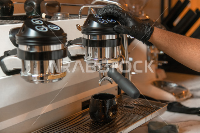 A Saudi Arabian Gulf man prepares coffee for customers in the cafe, makes hot coffee drink in the coffee machine, roasts and grinds fresh coffee, wear gloves, Saudi coffee shop