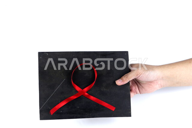 يد تمسك لوحة سوداء عليها شريط أحمر , شريط التوعية بمرض الإيدز , نقص المناعة البشرية , رعاية صحية , خلفية بيضاء .