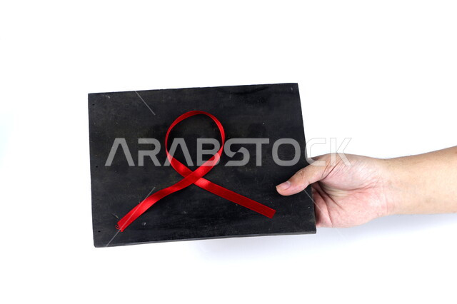يد تمسك لوحة سوداء عليها شريط أحمر , شريط التوعية بمرض الإيدز , نقص المناعة البشرية , رعاية صحية , خلفية بيضاء .