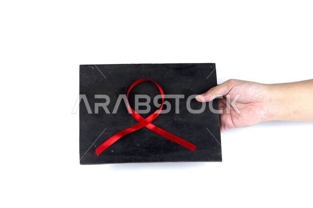 يد تمسك لوحة سوداء عليها شريط أحمر , شريط التوعية بمرض الإيدز , نقص المناعة البشرية , رعاية صحية , خلفية بيضاء .