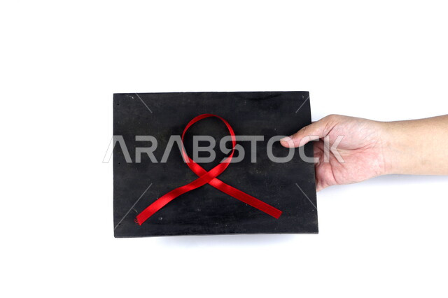 .A hand holding a black board with a red ribbon on it, AIDS awareness ribbon, HIV, health care, white background