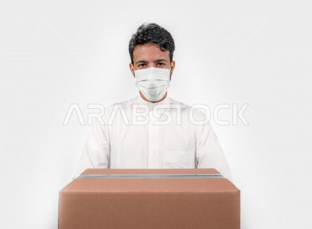 Portrait of a Saudi Arabian Gulf youth who follows prevention and safety measures by wearing a mask and hand gloves to avoid the spread of infection, delivering orders to the desired place, online orders, white background
