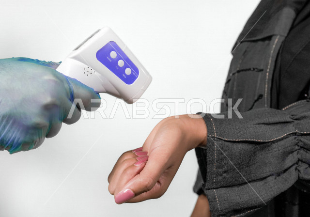 Close-up of a hand of a young Saudi Arabian Gulf woman, checking the temperature using a digital thermometer to measure the temperature by hand, following the prevention and safety measures against the Corona virus, white background