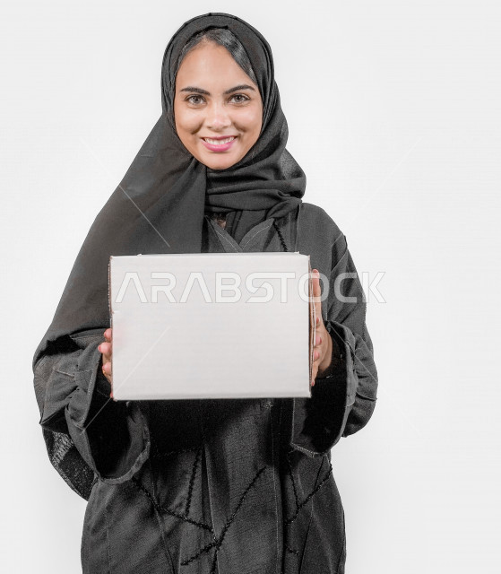 بورتريه لشابة عربية خليجية سعودية تقوم بإستلام صندوق الطلبات بإيماءات و تعابير تدل على السعادة ، طلبات اونلاين ، التسوق عن بعد ، مبيعات و مشتريات ، خلفية بيضاء