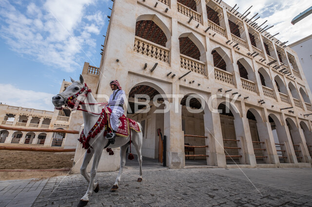 A Qatari Gulf Arab man riding an authentic Arabian horse, traditional Qatari dress, horse dressage, cultural activities and events, Souq Waqif in the State of Qatar, Qatar's historical monuments