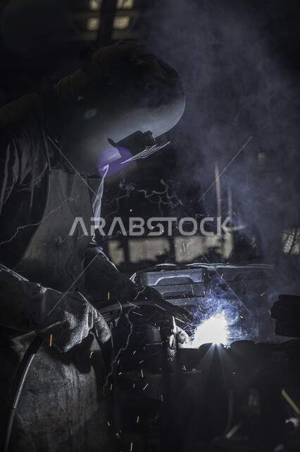 عامل عربي خليجي سعودي داخل مصنع الحديد ، ارتداء قناع الحماية في عمل لحام الحديد ، الحماية من شرارة لحام الحديد ، عملية انتاج الحديد .