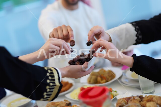 صورة مقربة لأيدي عائلة خليجية تتشارك حبات التمر على الافطار  ,  تجمع عائلي وقت الإفطار ,مناسبات دينية ، شهر رمضان المبارك   .