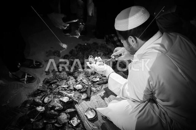 صورة بالابيض والاسود رجل عربي خليجي يعمل في استخراج اللؤلؤ الطبيعي من داخل أصداف المحار، مهن شعبية قديمة، حرفة استخراج اللؤلؤ، مهن وحرف يدوية