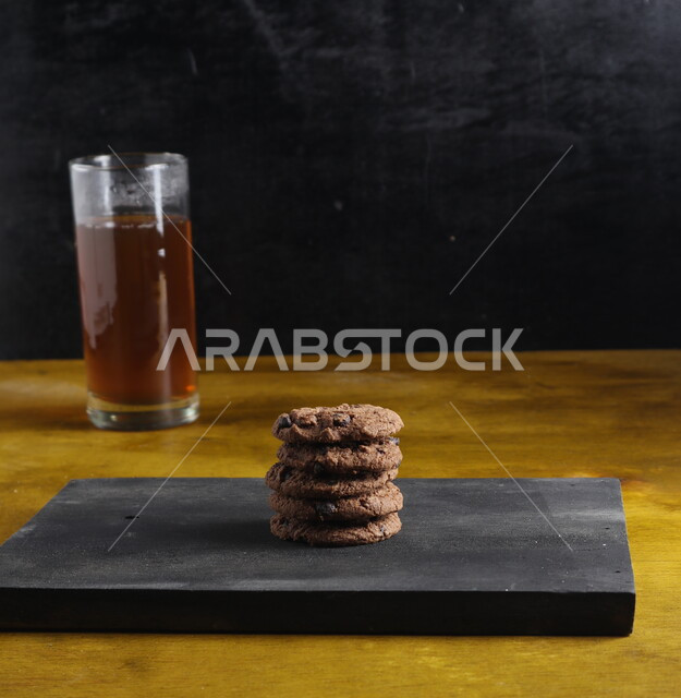 Hot chocolate chips with a cup of tea, biscuit chips with dark chocolate balls, cookies, baked sweets, black backgrounds 