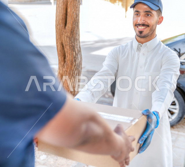 A young Saudi Arabian Gulf man wearing medical gloves to prevent corona virus, delivering orders to customers, safe and reliable delivery process, ordering products online, high quality shipping and delivery services