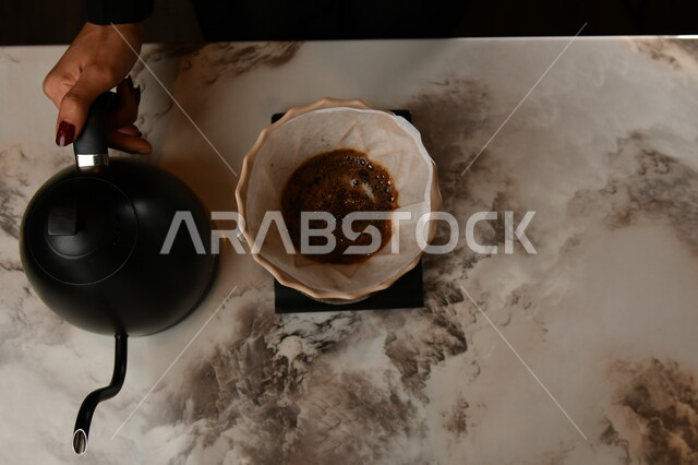 صورة مقربة من الاعلى ليد امرأة تسكب قهوة كيميكس الساخنة, قهوة مقطرة , كافيهات السعودية , باريستا , قهوة مختصة .