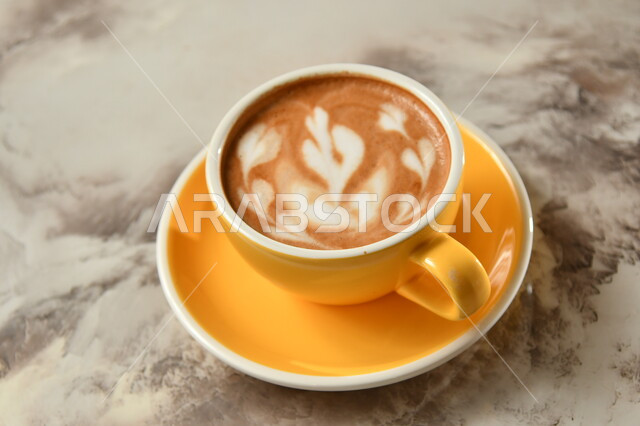 صورة مقربه فنجان قهوة برغوة كثيفة  مع رسومات ، مشروب الكابتشينو الساخن ، مشروبات ساخنة لذيذة ، فنجان القهوة الساخن, خلفية رمادية .