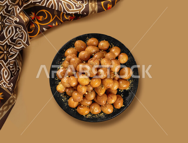 طبق  من حلا اللقيمات ، حلا شرقي ، حلويات وسكريات ، تحلية الزلابية  ،  وصفات وأطباق حلوى ,  مطاعم للمأكولات العربية الشرقية , خلفية بنية .