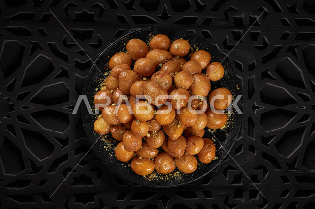 طبق  من حلا اللقيمات ،  حلويات وسكريات ، تحلية الزلابية  ، حلا شرقي ،  وصفات وأطباق حلوى ,  مطاعم للمأكولات العربية الشرقية , خلفية سوداء .