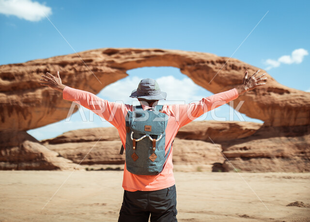 رجل عربي  يقف امام جبل القوس في مدينة العلا في المملكة العربية السعودية ,القوس الصخري في خشم أبو مخروق ، جبال طويق ,معالم جبلية في السعوديه, خلفية الطبيعه .