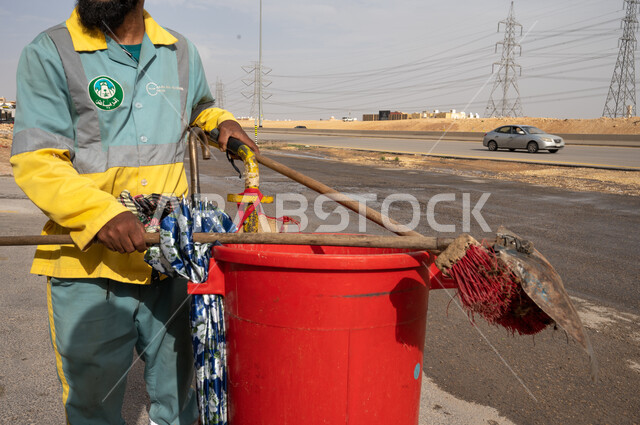 صورة مقربة لعامل النظافة أثناء العمل  ، عربة التنظيف وأدوات النظافة الخاصة بالعمل ، تنظيف الأبنية و الطرقات و الأرصفة ، الاهتمام بنظافة البيئة ، بلدية مدينة الرياض.