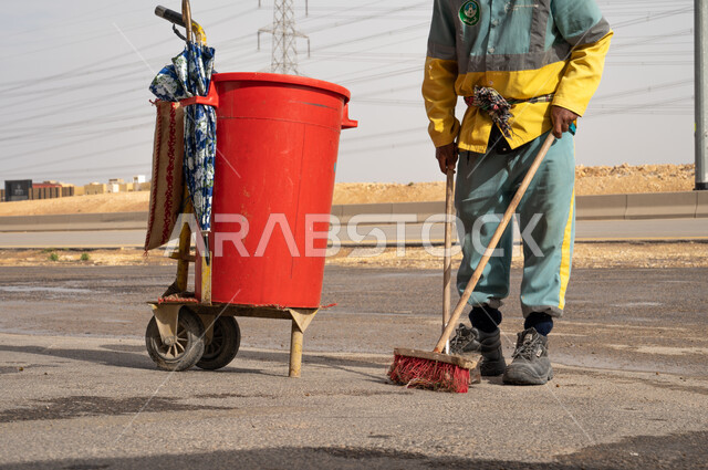 صورة مقربة لعامل النظافة أثناء فترة العمل  ، عربة التنظيف وأدوات النظافة الخاصة بالعمل ، تنظيف الأبنية و الطرقات و الأرصفة ، الاهتمام بنظافة البيئة ، بلدية مدينة الرياض.