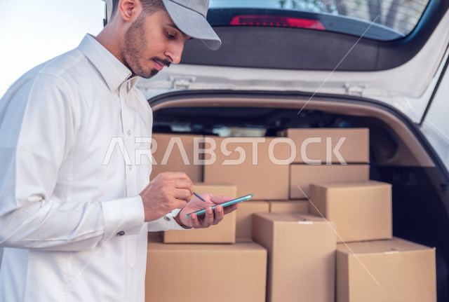شاب عربي سعودي خليجي يستخدم الهاتف المحمول  ، فحص الطرود والطلبات من خلال الجهاز المحمول ، تحديد موقع التوصيل ، عملية توصيل الطلبات للزبائن ،  التسوق وطلب المنتجات عبر الإنترنت ،  خدمات الشحن و التوصيل ذات الجودة العالية