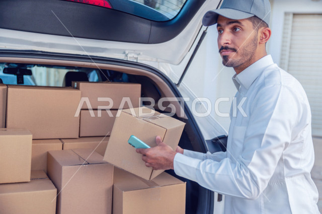 A young Saudi Arabian Gulf man using a mobile phone, checking parcels and orders through the mobile device, determining the delivery location, the process of delivering orders to customers, shopping and ordering products online, high-quality shipping and