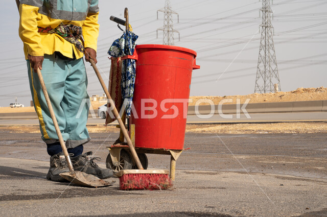 صورة مقربة لعامل النظافة أثناء فترة العمل ، إزالة النفايات الطريقية والاهتمام بنظافة البيئة ، عربة التنظيف  وأدوات النظافة الخاصة بالعمل ، بلدية مدينة الرياض.