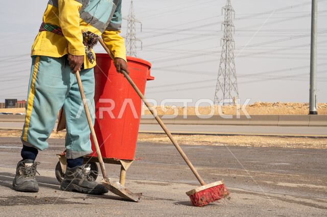 صورة مقربة لعامل النظافة أثناء فترة العمل ، إزالة النفايات الطريقية والاهتمام بنظافة البيئة ، عربة التنظيف  وأدوات النظافة الخاصة بالعمل ، بلدية مدينة الرياض.