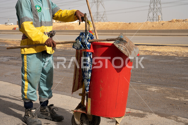 صورة مقربة لعامل النظافة أثناء فترة العمل ، تنظيف الأبنية و الطرقات  والاهتمام بنظافة البيئة ، عربة التنظيف  وأدوات النظافة الخاصة بالعمل ، بلدية مدينة الرياض.