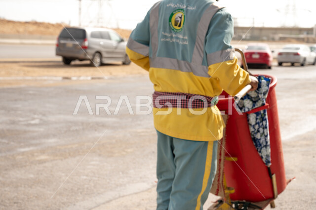 عامل النظافة بصورة مقربة  باللباس الخاص بالعمل ، تنظيف  الطرقات والأرصفة  والاهتمام بنظافة البيئة ، عربة التنظيف  وأدوات النظافة الخاصة بالعمل ، بلدية مدينة الرياض.