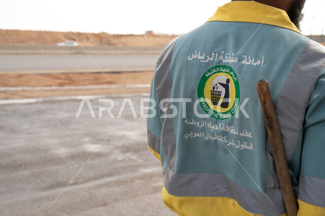 عامل النظافة  باللباس الخاص بالعمل بصورة مقربة  ، تنظيف الطرقات والأرصفة  والاهتمام بنظافة البيئة ، عربة التنظيف وأدوات النظافة الخاصة بالعمل ، بلدية مدينة الرياض.