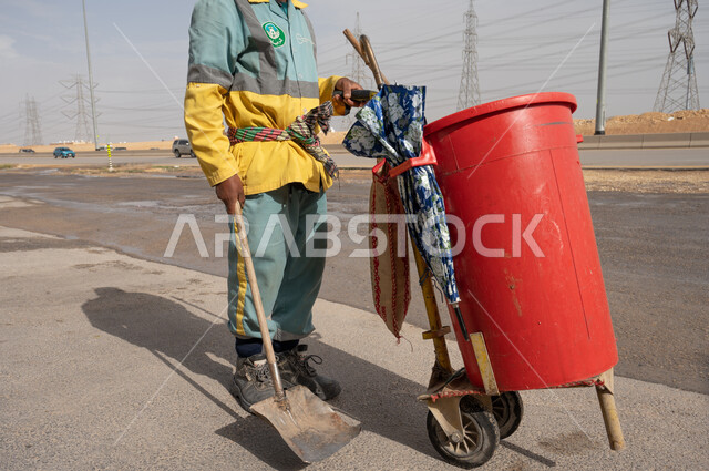 عامل النظافة أثناء فترة العمل ، تنظيف الطرقات والأرصفة  والاهتمام بنظافة البيئة ، عربة التنظيف وأدوات النظافة الخاصة بالعمل ، بلدية مدينة الرياض.