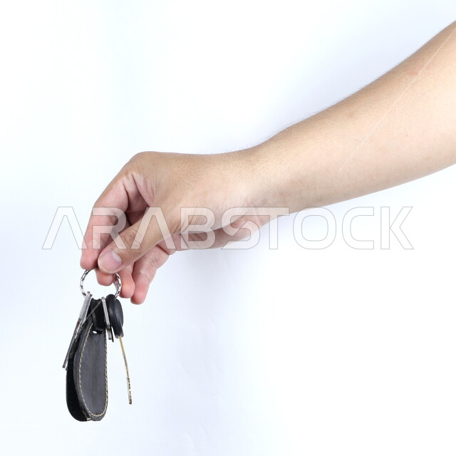 صورة مقربة ليد تمسك مجموعة من المفاتيح  , علاقة مفاتيح ,  سلسلة نحاسية دائرية للمفاتيح , خلفية بيضاء .