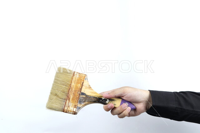 صورة مقربة ليد تمسك فرشاة دهان  , فراشي و ادوات طلاء , رسم وفنون , مهن وحرف يدوية  , خلفية بيضاء .