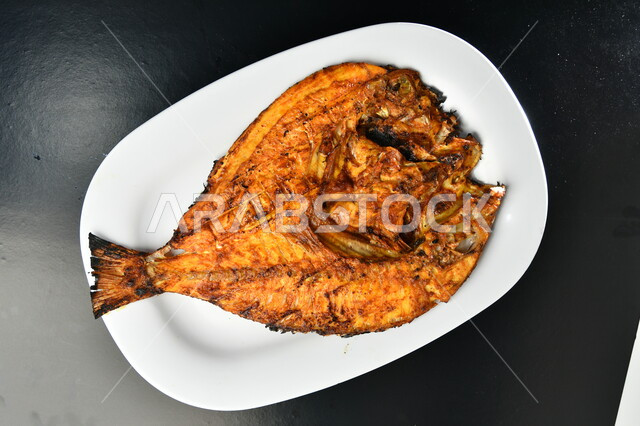 طبق من السمك المقلي المتبل مع الخضار ، مأكولات بحرية عربية ، وجبة طعام غذائية صحيه ، أطباق ووصفات شرقية , خلفية سوداء  .