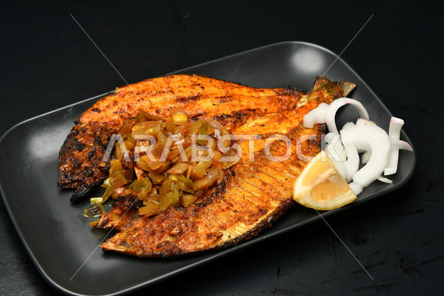 طبق من السمك المقلي المتبل مع الخضار ، مأكولات بحرية عربية ، وجبة طعام غذائيه صحية ، أطباق ووصفات شرقية , خلفية سوداء  .