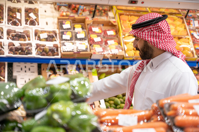رجل عربي سعودي خليجي في قسم الخضراوات والفواكه  داخل السوبرماركت ، الاحتياجات المنزلية ، السلع والمواد الغذائية  ، عربة التسوق.