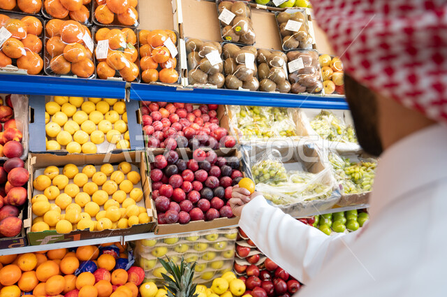 صورة مقربة لرجل عربي سعودي خليجي في قسم الخضراوات والفواكه   ، الاحتياجات المنزلية ، السلع والمواد الغذائية  ، عربة التسوق.