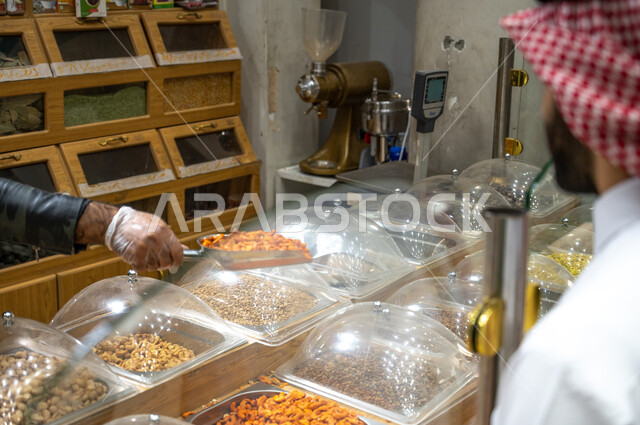 رجل عربي سعودي خليجي  في المتجر يقوم  بشراء المكسرات والتسالي  ، وجبة خفيفة ، السلع والمواد الغذائية المختلفة ، مستلزمات المستهلك.