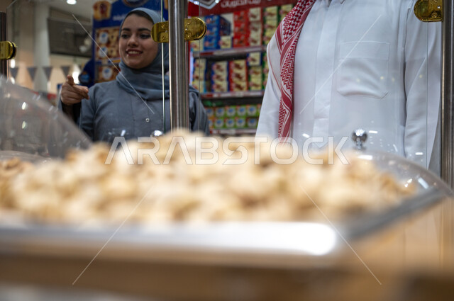 زوجان عربيان سعوديان في متجر المكسرات داخل السوبرماركت ، مكسرات صحية ، وجبة خفيفة ، السلع والمواد الغذائية المختلفة ، مستلزمات المستهلك.