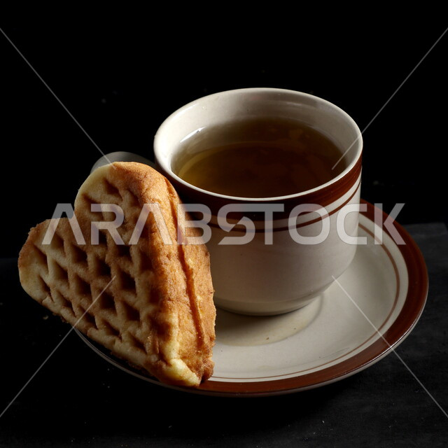 صورة مقربة لكوب الشاي مع قطعة البسكويت اللذيذة، مشروبات ساخنة، وجبة افطار خفيفة، قطعة من الحلوى الشهية، خلفية سوداء