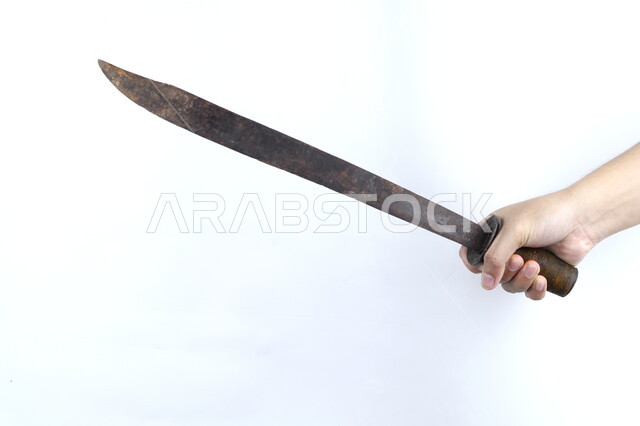 صورة مقربة ليد رجل يمسك بساطور معدني، سيف صدئ، منجل قديم، مقبض خشبي، اسلحة قديمة، خلفية بيضاء