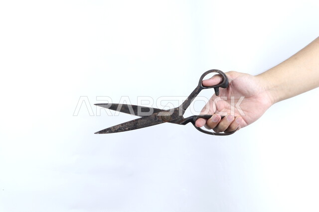 صورة مقربة ليد رجل يمسك بمقص معدني قديم، ادوات الخياطة، مقبض بلاستيكي، خلفية بيضاء