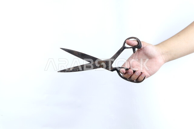 صورة مقربة ليد رجل يمسك بمقص معدني، ادوات الخياطة، مقبض بلاستيكي، مقص قديم، خلفية بيضاء