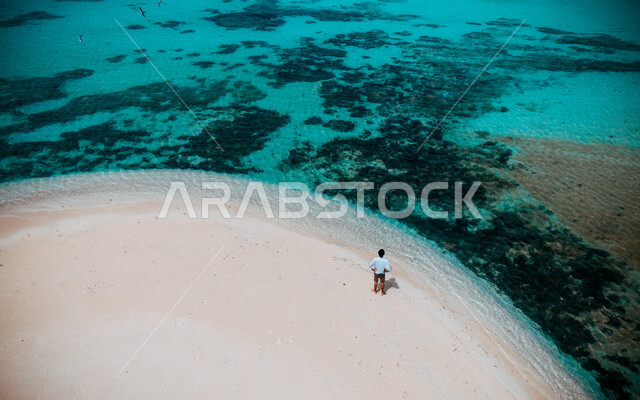 صورة من الاعلى لرجل يقف على شاطئ جزيرة سمر في عسير في المملكة العربية السعودية، رمال البحر البيضاء، اماكن ساحلية، شاطئ البحر، سواحل البحر الاحمر، السياحة في السعودية