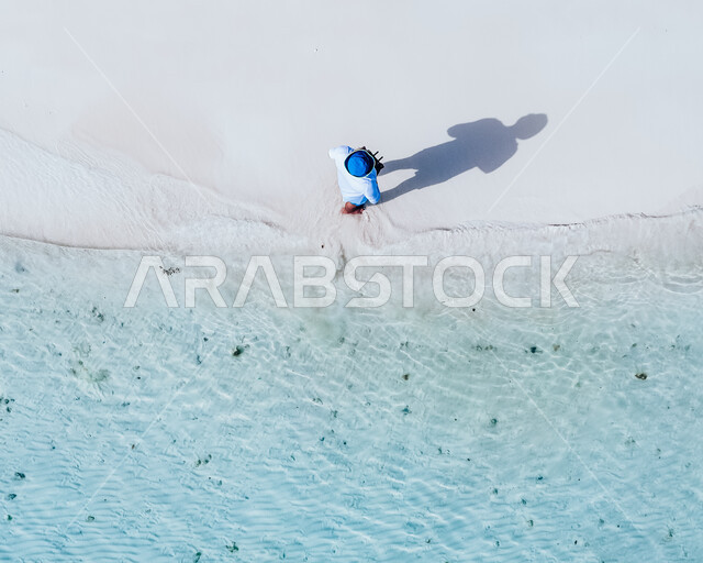 A picture from above of a man walking on the seashore, white sand, natural scenery, tourist places