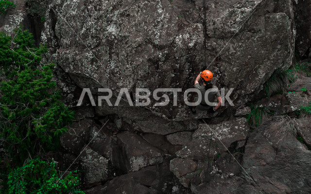 A Saudi Arabian Gulf man practicing mountaineering, Al-Soudah Mountains in Abha, Asir in the Kingdom of Saudi Arabia, Asir landmarks, rocky mountain climbing, mountain nature