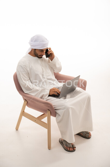 بورتريه لرجل عربي خليجي إماراتي يجلس على كرسي يستخدم جهاز الحاسوب، اجراء مكالمات هاتفية ، تواصل اجتماعي،  التواصل مع الأصدقاء، اجتماع عمل عن بعد ، محادثات ودردشة ، خلفية بيضاء .